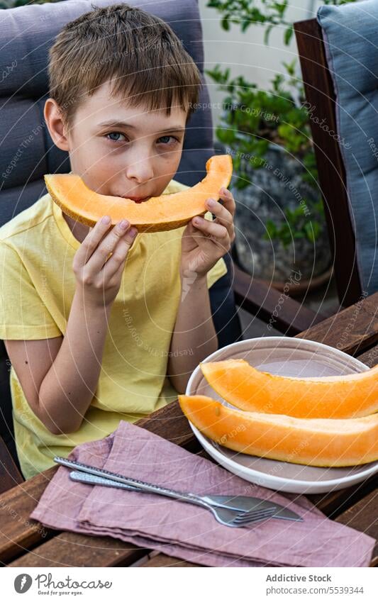 Preteen boy sitting at table and eating fresh cut musk melon preteen fruit healthy slice nature summer child refreshment drink beverage food kid breakfast