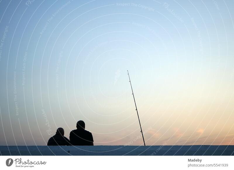 Anglers in the romantic light of the setting sun in the evening at the marina of Altinoluk on the Gulf of Edremit on the Aegean Sea in the province of Balikesir in Turkey