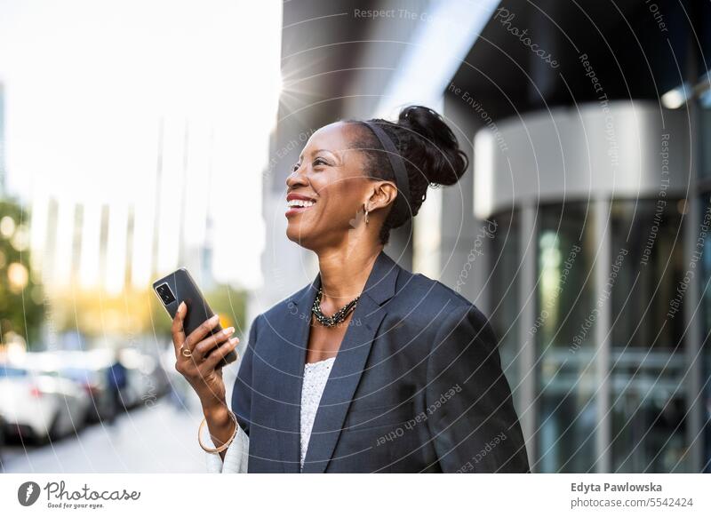 Portrait of smiling mature businesswoman using mobile phone in urban setting people downtown joy black natural attractive city black woman happiness street