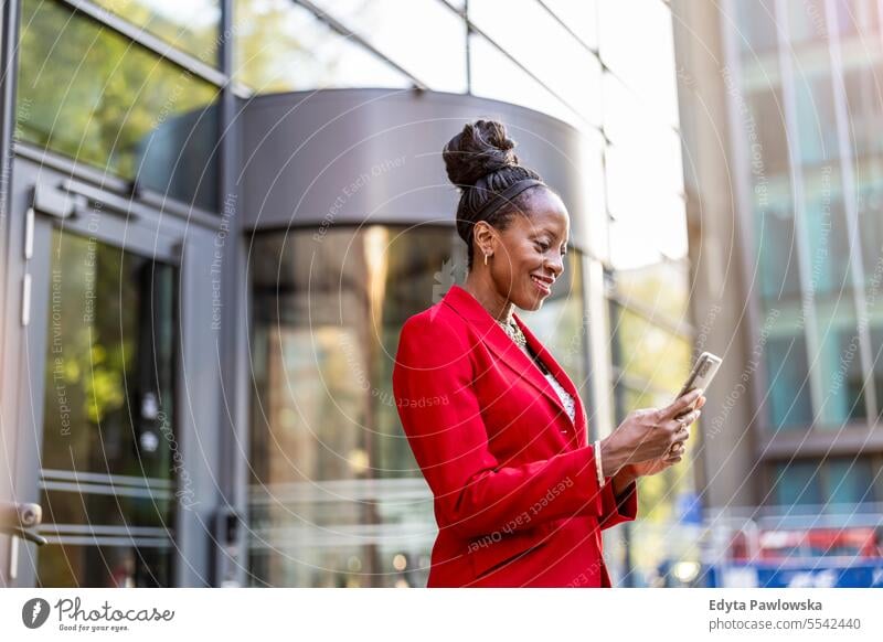 Portrait of smiling mature businesswoman using mobile phone in urban setting people downtown joy black natural attractive city black woman happiness street