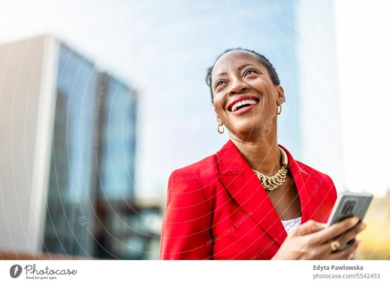 Portrait of smiling mature businesswoman using mobile phone in urban setting people downtown joy black natural attractive city black woman happiness street