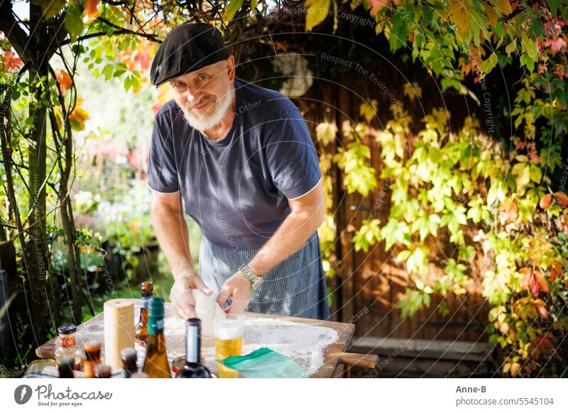 Pizza season in the garden is slowly coming to an end. Friendly man with beard kneading dough , around him wild vine in the beginning of autumn color. selfmade