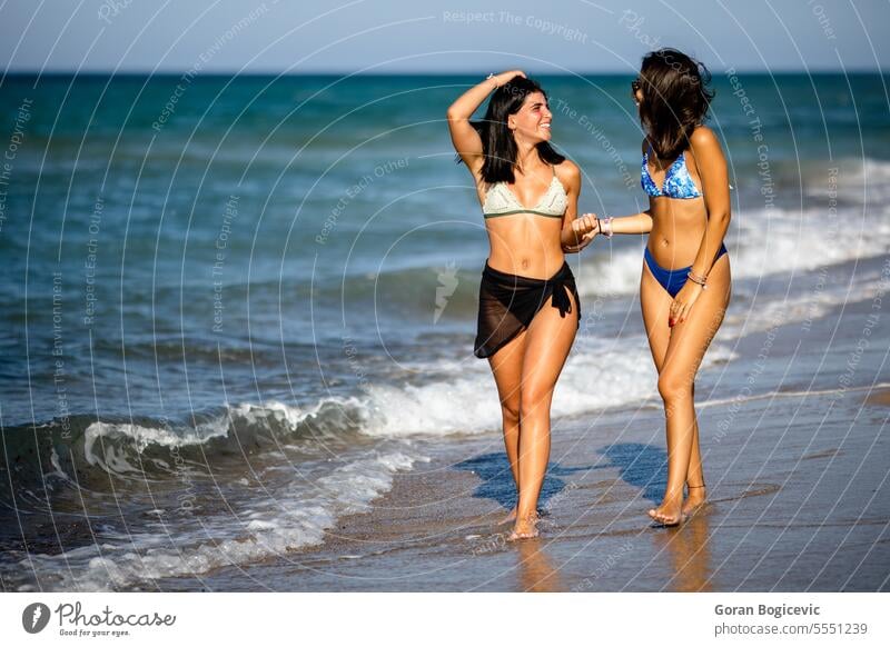 Two pretty young woman having fun on the seaside summer female bikini friends beach vacation swimwear together people happiness sand happy ocean water cheerful