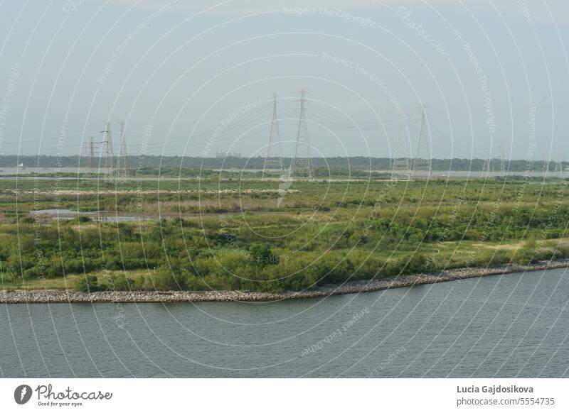 High electric pylons on a green field observed from the container terminal of the Port of Houston. background blue cable coast electrical electricity energy