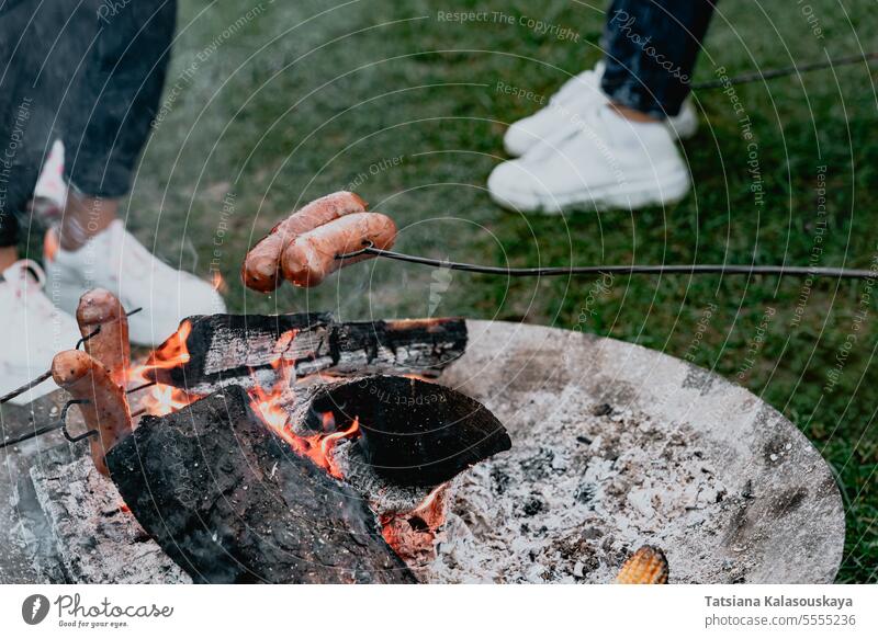 A group of friends roasts sausages on metal skewers on a fire food grill picnic bonfire heat flame barbecue meat cooking hot leisure summer meal camp weekend