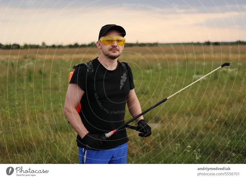 Farmer in protective glasses and gloves with mist sprayer treats potato plantation from pests, colorado beetle and fungus infection and looks at camera. Harvest processing. Protection and care harvest