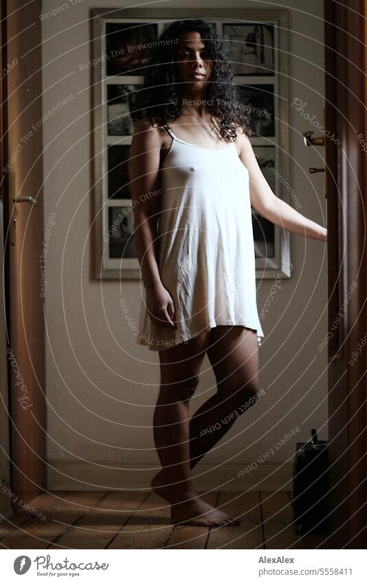 A young beautiful woman stands in the hallway of an apartment dressed in a shirt Woman Young woman Long-haired Curly pretty Athletic Slim Legs Barefoot Room