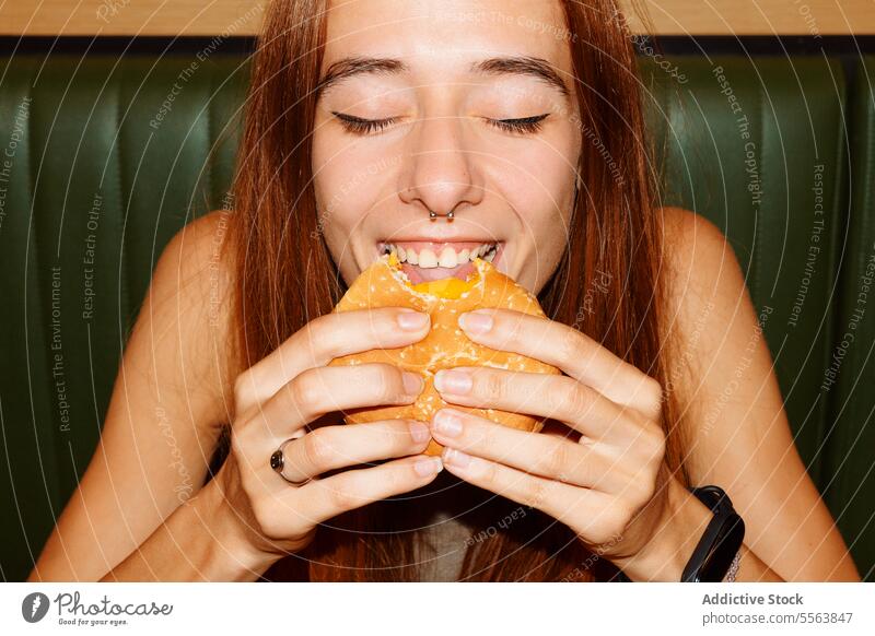 Young woman enjoy eating hamburger girl fast food young table sitting one dinner lunch snack holding hand unhealthy nutrition indoors restaurant redhead