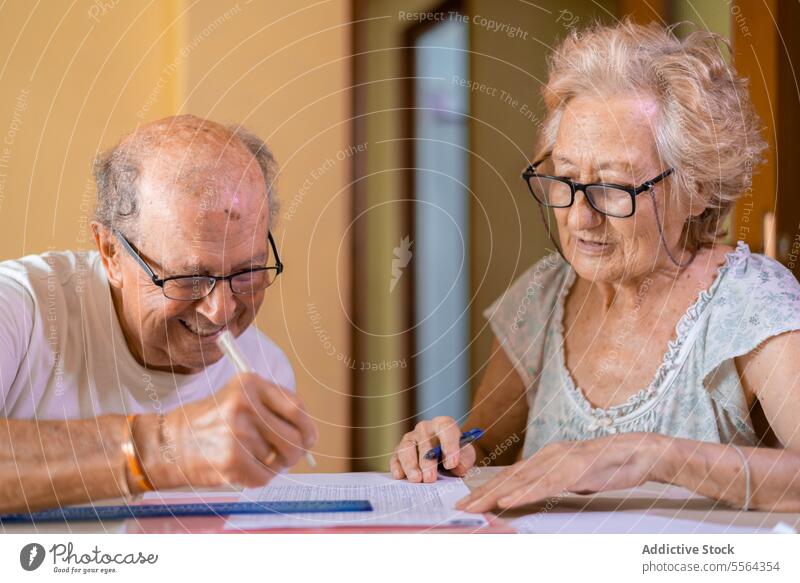 Grandparents doing memory exercises at home grandparents grandfather grandmother eyeglasses sit table chair practice focus concentrate work looking down house