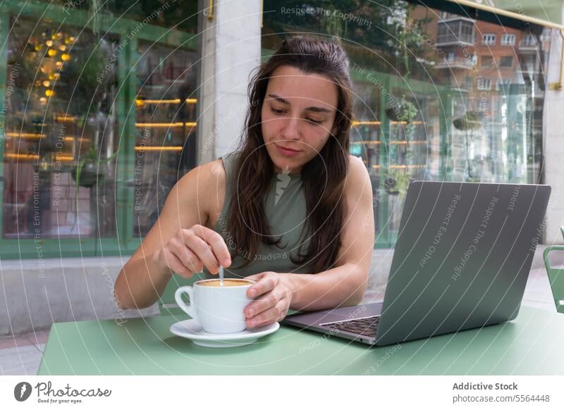 Woman adding sugar in cup of coffee in cafe woman freelance remote internet startup laptop work happy smile workplace female online browsing surfing gadget