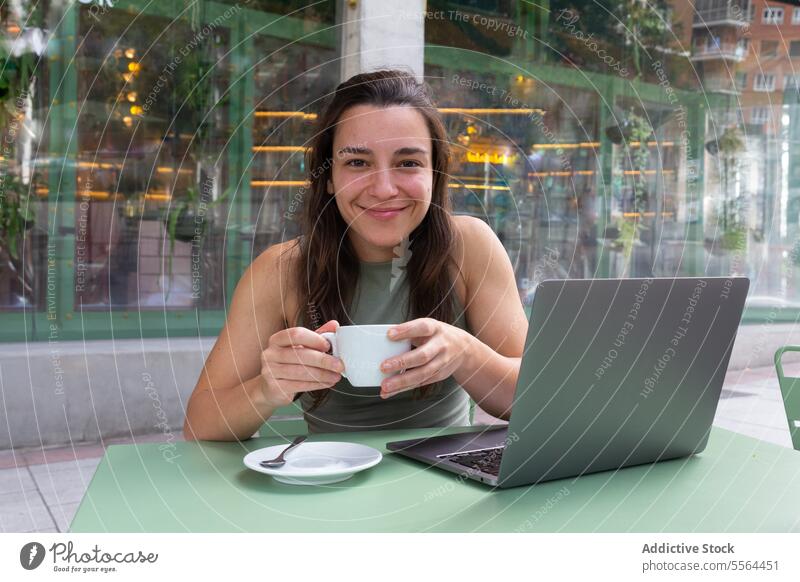 Young freelancer drinking hot coffee in cafe woman remote work smile happy laptop gadget young table hot drink female people internet computer entrepreneur