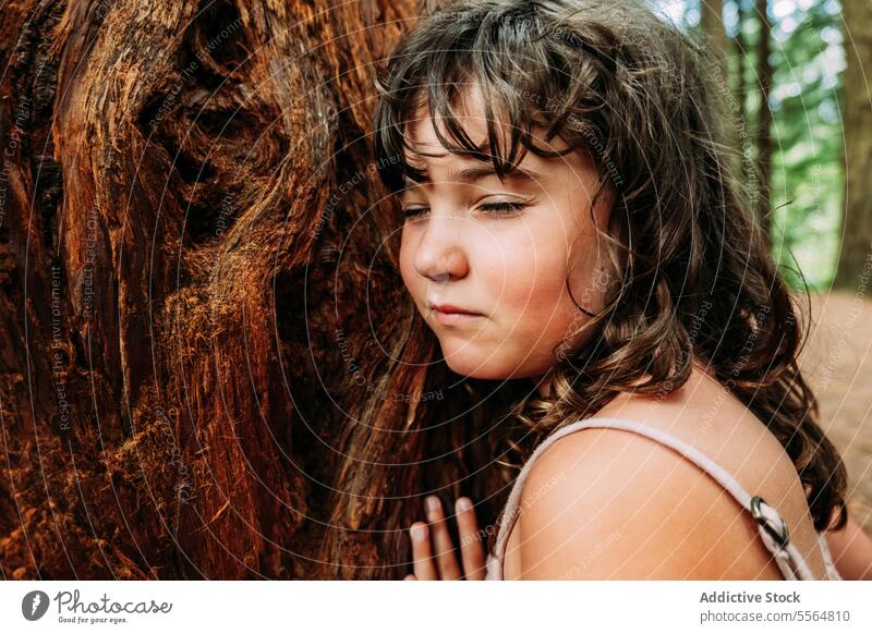 Calm little girl touching old tree trunk in forest nature cute adorable child kid childhood daytime joy love tranquil harmony environment peaceful innocent calm