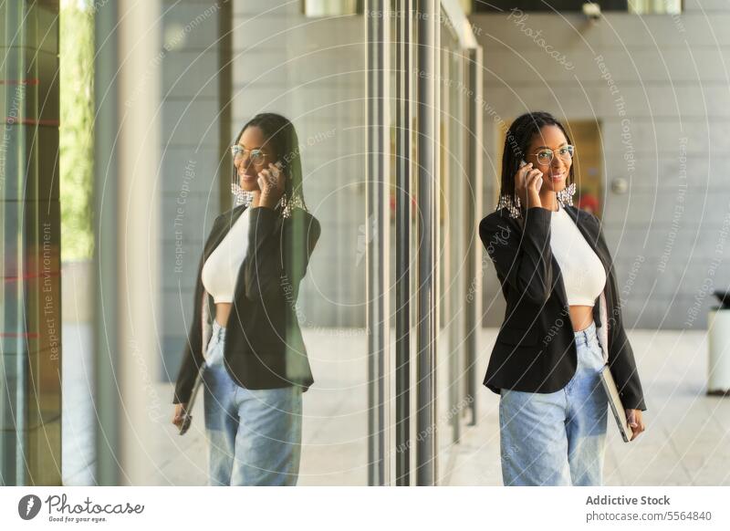 Smiling businesswoman walking and talking on mobile phone while holding laptop smartphone entrance speak smile entrepreneur modern office doorway using