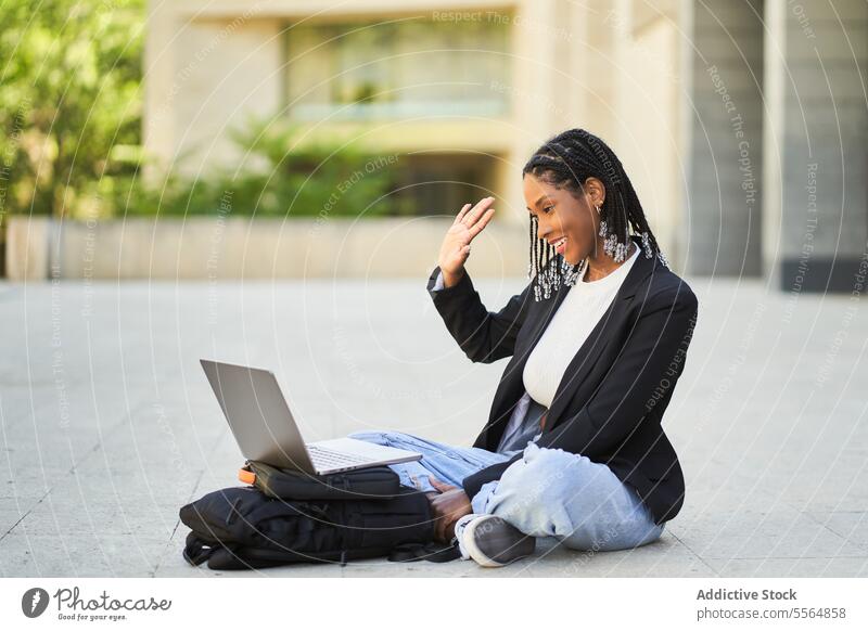 Smiling African American businesswoman talking via laptop pc street using smartphone device video chat communicate speak online entrepreneur connection netbook