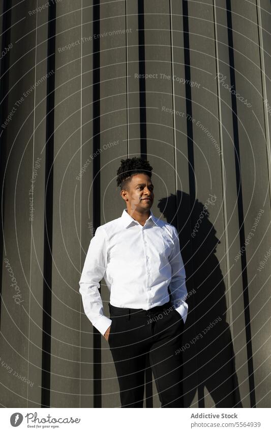 Stylish black man in white shirt standing against dark metallic wall positive confident style formal office hand in pocket dreadlocks street seamless pattern