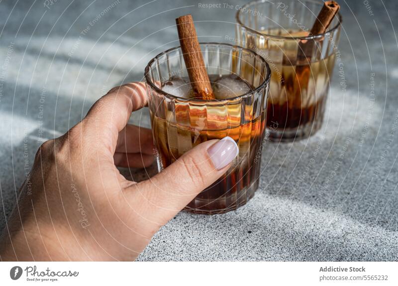 Hand holding apple cider drink hand cocktail cinnamon stick anise star slice glass cube finger nail beverage alcohol refreshment garnish serve fruit transparent