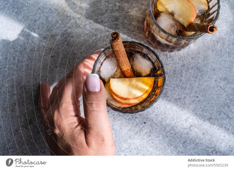 Hand holding apple cider drinks hand cocktail cinnamon stick anise star slice glass cube finger nail beverage alcohol refreshment garnish serve fruit