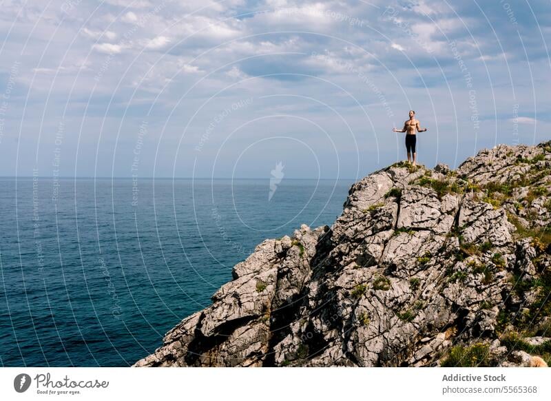 Man doing yoga on a seaside cliff pose balance fitness health meditation tranquility rocks coast concentration flexibility nature outdoors workout strength