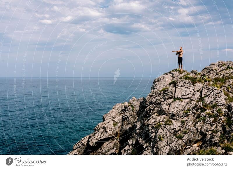 Man doing yoga on a seaside cliff pose balance fitness health meditation tranquility rocks coast concentration flexibility nature outdoors workout strength