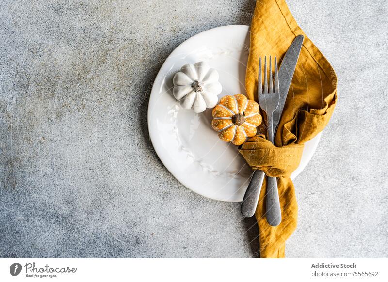 Decorative pumpkin plate setting decoration fork knife napkin mustard ceramic silver texture gray surface autumn festive tableware dining design fall