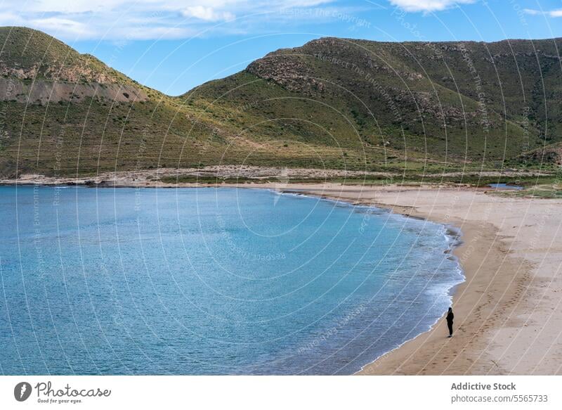 Woman on the shore of a beach next to mountains sea nature mediterranean seascape coastline travel sand vacation outdoor rock water tourism travel destination