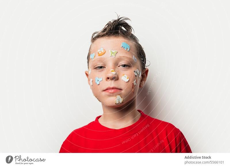 Boy with animal stickers on face boy wet hair red shirt white background child playful fun portrait close-up expression cute youth innocence style modern