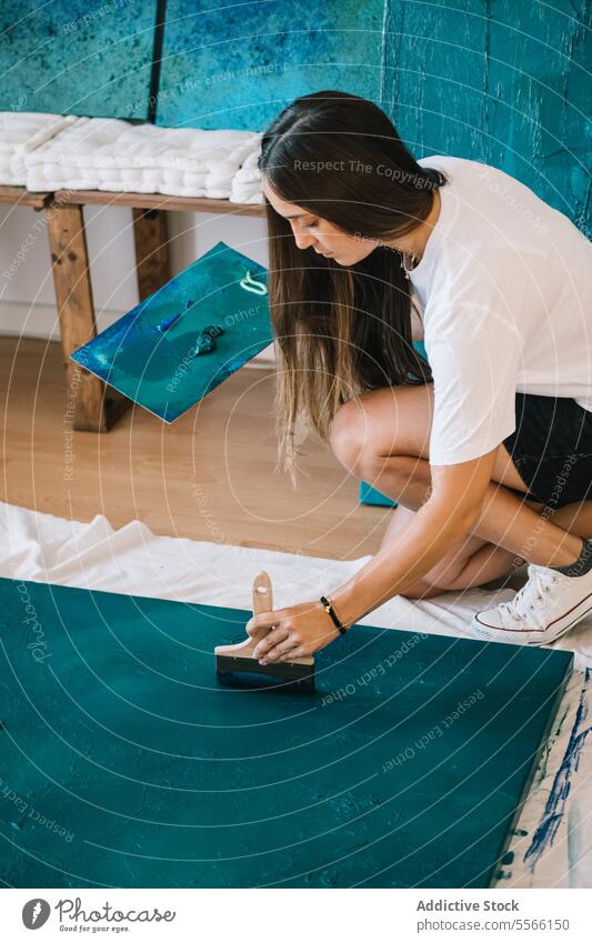 Concentrated female artist painting on floor with oil paint and brush in studio woman paintbrush draw talent concentrate creative painter casual create