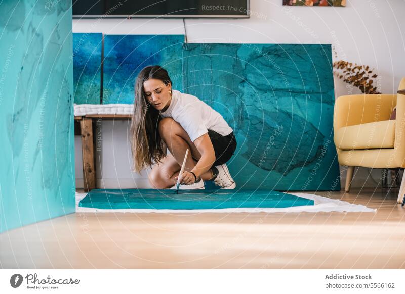 Concentrated female artist painting on floor with oil paint and brush in studio woman paintbrush draw talent concentrate creative painter casual create