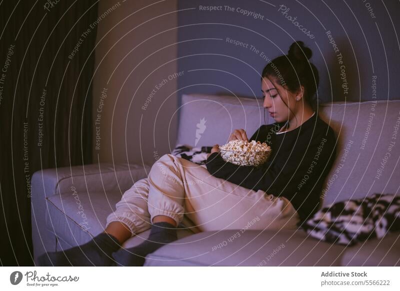 Young woman resting on comfortable sofa with popcorn bowl in living room relax sock light at home female young sit jacket sleeve cozy couch free time weekend