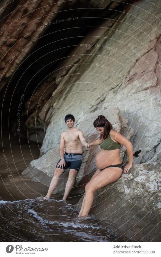 Man and pregnant woman resting on rough mountain near sea shore stone lean water summer female nature coast relax pregnancy mother tummy prenatal motherhood