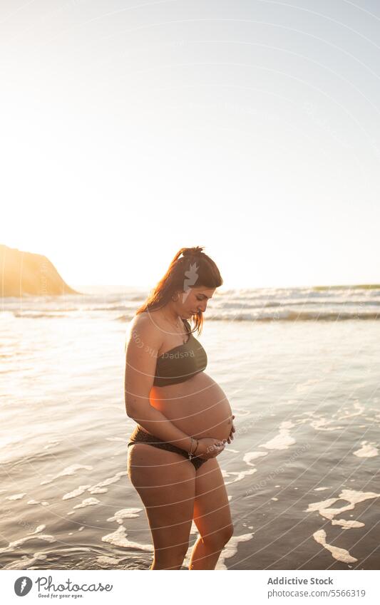 Pregnant woman standing in sea water pregnant belly expect bikini summer sunset await touch female happy cheerful smile prenatal anticipate pregnancy maternal