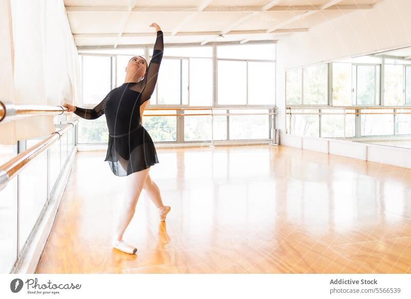 Dancer poise in bright studio ballet dancer barre light window grace focus arm extend pointe shoe balance female elegance form pose performance art discipline