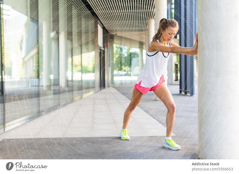 A woman in a white tank top and pink shorts stretching fitness active exercise workout sport health wellness athlete flexibility gym active wear athletic street