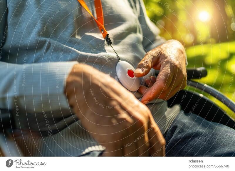 Senior man pressing Alarm Button in a wheelchair outside in a park, closeup. Emergency call system concept image. hand medical alarm system emergency call