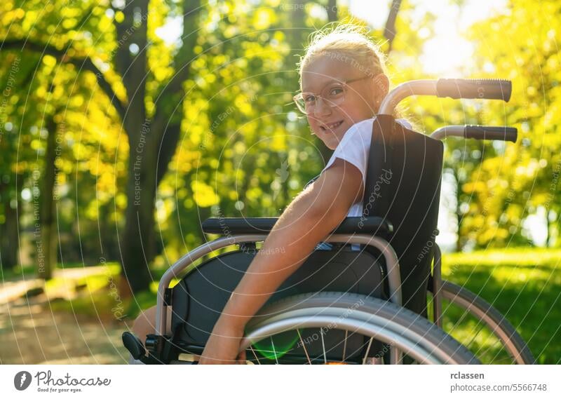 Smiling young handicapped blond girl sit in wheelchair during walk in park, teenager disability concept image happy paralysis care physical help support therapy