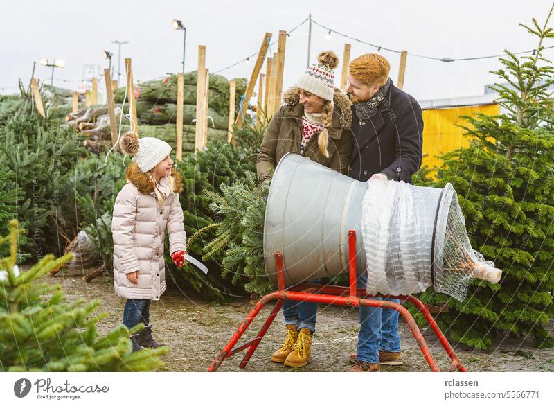 Family stand at a wrapping machine for a cut Christmas tree at a street market teamwork buy help child daughter safety net pack bagged bind christmas season