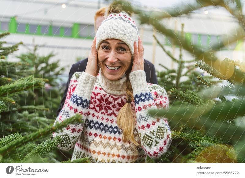 Happy woman and her Boyfriend at a market want to buy a Christmas tree and look into the camera surprised family happy skeptical redhead tradition choice smile