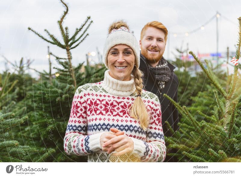 Happy couple at a market want to buy a Christmas tree and look into the camera looking surprised family happy redhead tradition choice smile man love couple