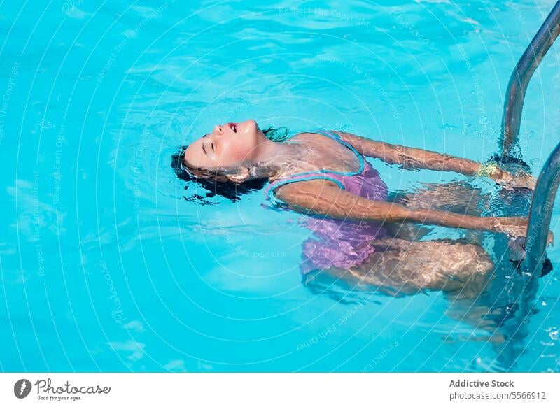 Child floating in pool clinging to ladder. child blue swimsuit purple grace peace summer water hold metal relax fun beauty tranquility outdoor leisure grip