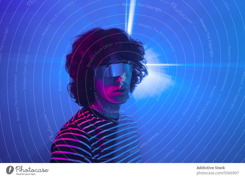 Latin man with futuristic glasses bathed in blue light curly hair striped virtual reality vr shirt metaverse latin purple setting illuminate fashion model tech