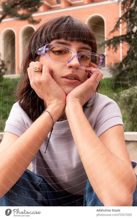 Modern woman sitting on park and leaning face on hands personality confident style posture cool freedom female carefree serious accessory individuality gaze