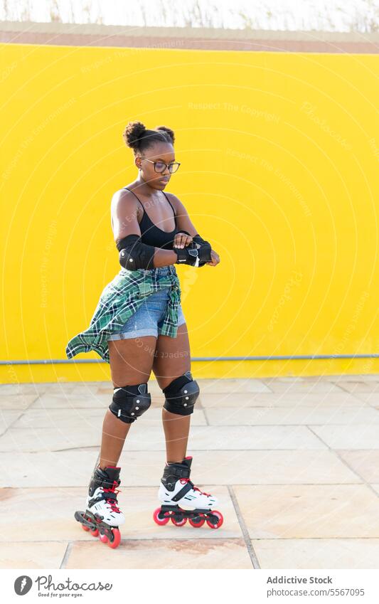 Young Female Fixing Hand Gear While Rollerskating At Skate Park Woman Skating Fasten Casual Wall Yellow Sport Practice Leisure Weekend Activity Summer Lifestyle