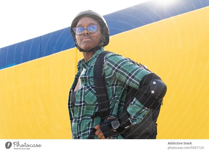 Thoughtful Woman In Helmet And Eyeglasses Standing At Skate Park Looking Away Sunlight Protection Gear Backpack Casual Wall Yellow Plaid Shirt Sport Leisure