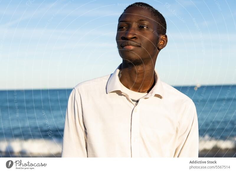 Young man contemplating the beach ocean horizon shirt white young calm serene portrait gaze contemplative sky blue water shore coastline sea waves tranquil