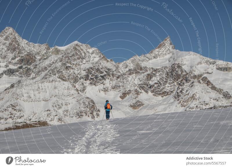 Person with ski poles on snowcapped mountain during vacation full body back view unrecognizable person walking covering sunny adventure day swiss alps hiking