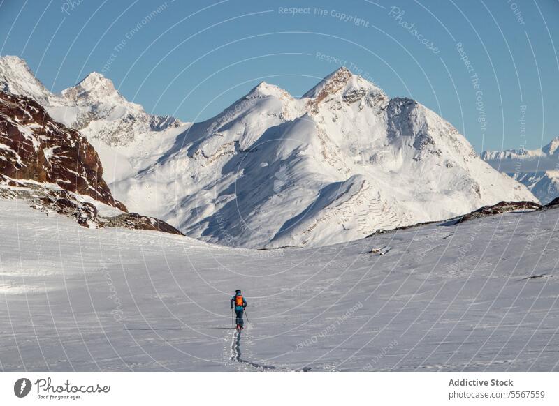 Person with ski poles on snowcapped mountain during vacation full body back view unrecognizable person walking covering sunny adventure day swiss alps hiking