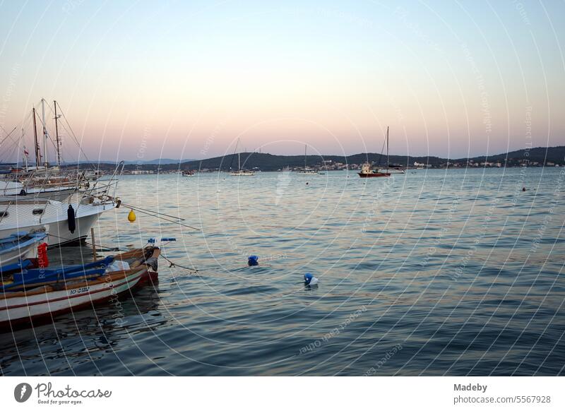 Romantic evening atmosphere by the sea with boats and yachts in the light of the evening sun with lighthouse and pier at the harbor in the bay of Ayvalik on the Aegean Sea in the province of Balikesir in Turkey