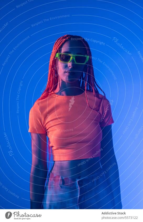 Woman with orange braids standing in neon lights woman young portrait metaverse afro braids abstract serious confident individuality appearance sunglasses