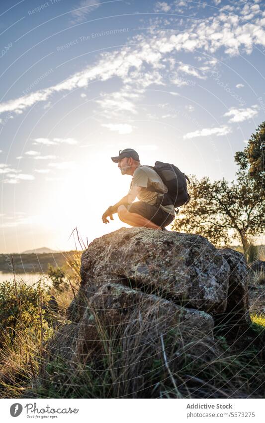 Man resting on boulder at sunset in Pantano de Layos man traveler rock Toledo Spain lookout landscape hiker trekking nature outdoor explore water backpack