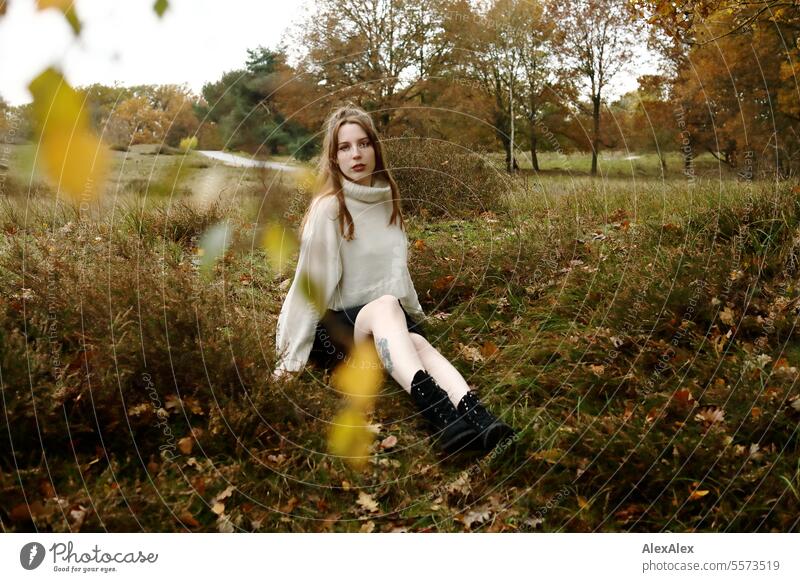 Young woman in white wool sweater and black skirt sits in the grass between heather in a northern German heath landscape in fall Woman Large tall woman